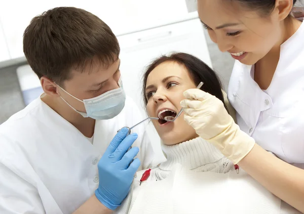 Νεαρή γυναίκα, κρατώντας το στόμα ανοικτό ενώ οδοντίατρος εξετάζει — Φωτογραφία Αρχείου
