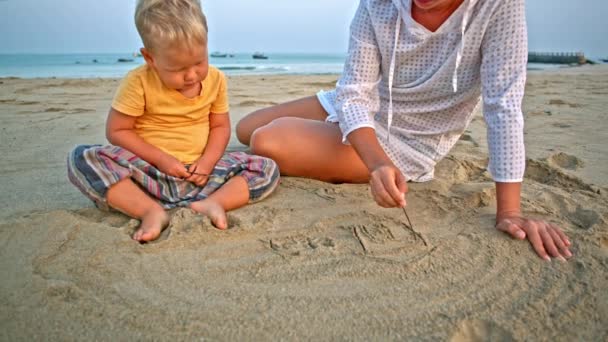 Baby und Mutter zeichnen im Sand am Strand — Stockvideo