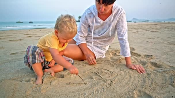 Bebé y madre dibujan en la arena en la playa — Vídeos de Stock