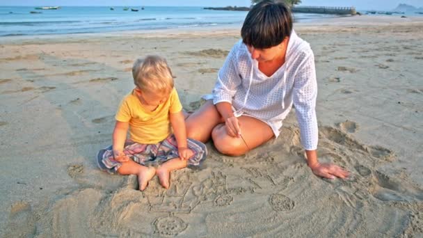 Baby en moeder teken in zand op strand — Stockvideo