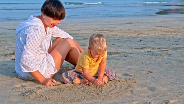 Bebé y madre dibujan en la arena en la playa — Vídeos de Stock