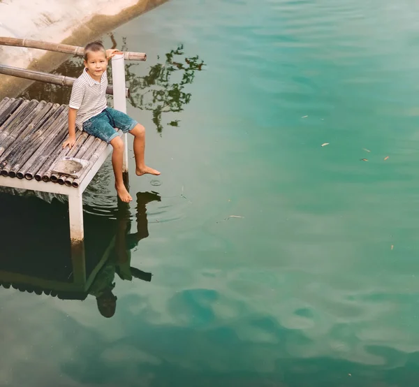 一个可爱的小男孩坐在湖上的防波堤上的户外肖像 免版税图库图片