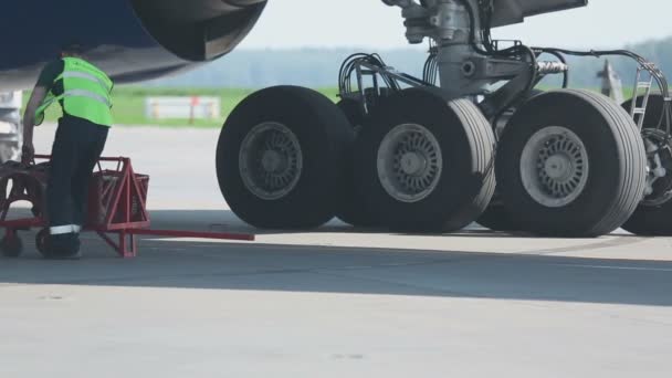 Сотрудник аэропорта устанавливает прокладки под шасси стоянки самолетов — стоковое видео