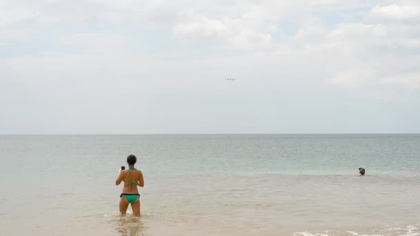 Menschen am Strand von Mai Khao schwimmen im Meer und beobachten Flugzeuge, die auf dem Flughafen von Phuket landen. — Stockvideo