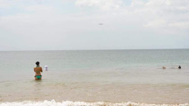 Ludzie na plaży Mai Khao pływają w morzu i obserwują samoloty lądujące na lotnisku Phuket. — Wideo stockowe