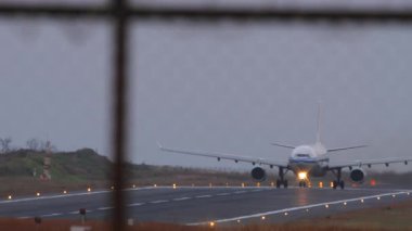 Pistte tanınmayan bir üniforması olan bir jet yolcu uçağı, ön taraftaki çitten görülüyor.