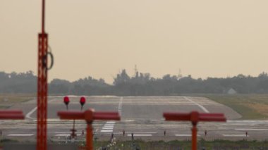 Sıcak akşam ışığı altında boş bir havaalanı pisti. Asfalt üzerinde görünen ısı sisi, ışıltılı bir etki yaratıyor. Ufukta beliren pist işaretlerinin ve yaklaşan ışıkların görüntüsü