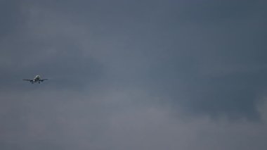 Bulutlu ve karanlık bir gökyüzünde yaklaşan bir jet yolcu uçağının uzun çekim görüntüleri.
