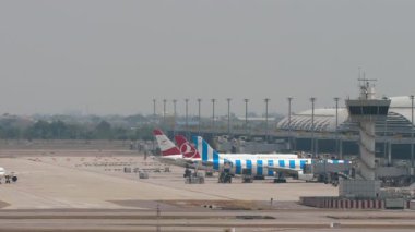 BANGKOK, THAILAND - 15 Mart 2025: Airplane Spring Airlines Airbus A320, B-6863 Suvarnabhumi Havaalanı 'nda taksicilik. Terminalde sıra sıra bekleyen uçaklar. Arka planda başka bir uçak kalkıyor..