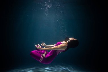 Kız, suyun altında spor kıyafetleriyle yoga yapıyor. Meditasyona daldırma