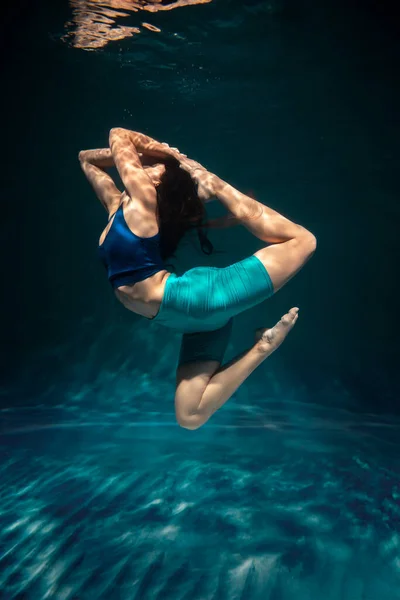 A menina está envolvida em ioga sob a água em roupas esportivas. Asanas e meditação Imagem De Stock
