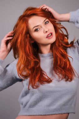 Genç ve çekici kızıl saçlı kız kameraya bakıp gülümsüyor.