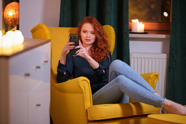 Красивая девушка использует свой смартфон на диване дома в гостиной