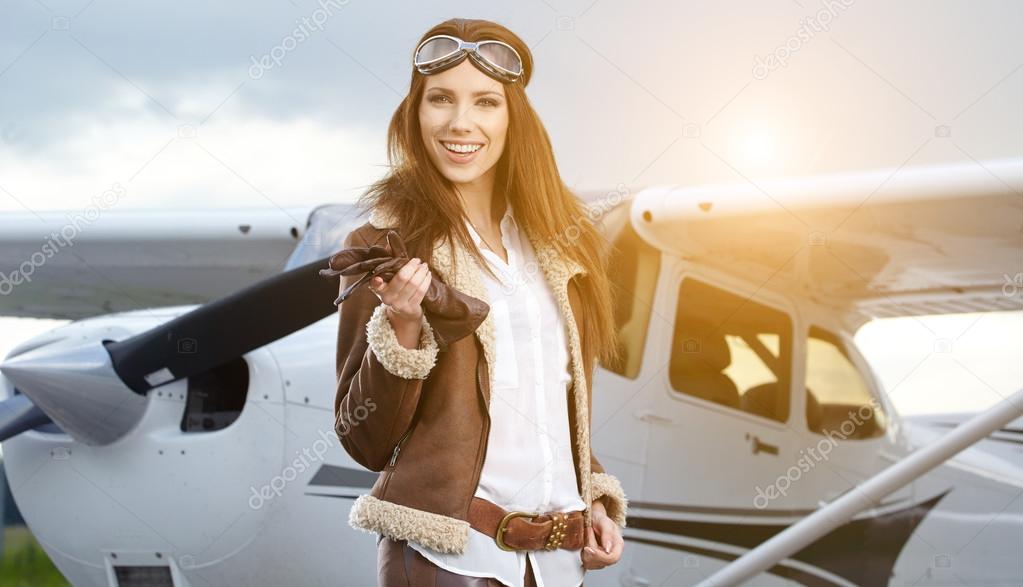 Portrait of young beautiful woman pilot in front of airplane. 