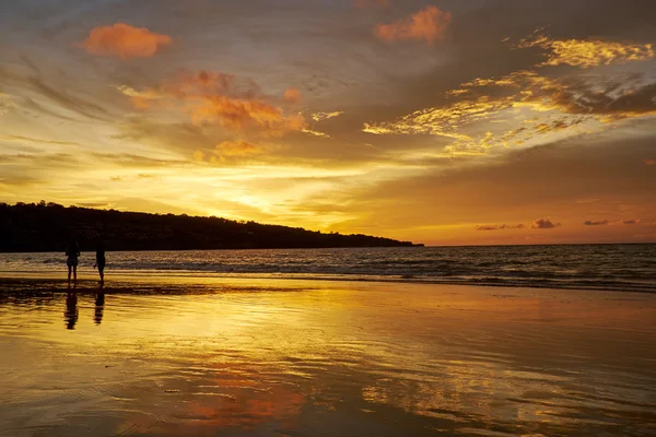 Siluetas de parejas en la playa al atardecer — Foto de Stock