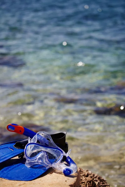 Mascarilla y aletas en una playa de rocas — Foto de Stock