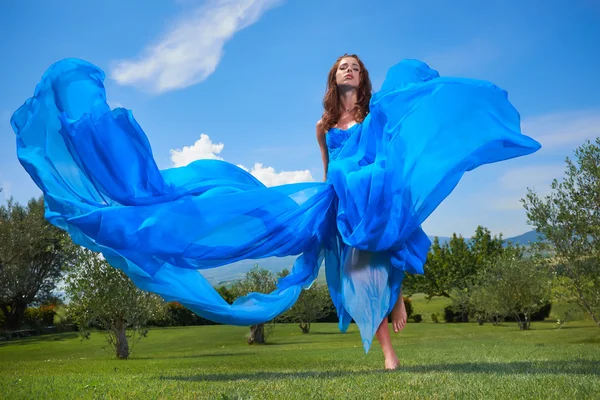 Vrouw in blauwe jurk poseren met hemel op achtergrond — Stockfoto