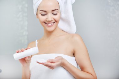 Kadın Wrapped ile banyo havlusu, yüzünde krem uygulamak 