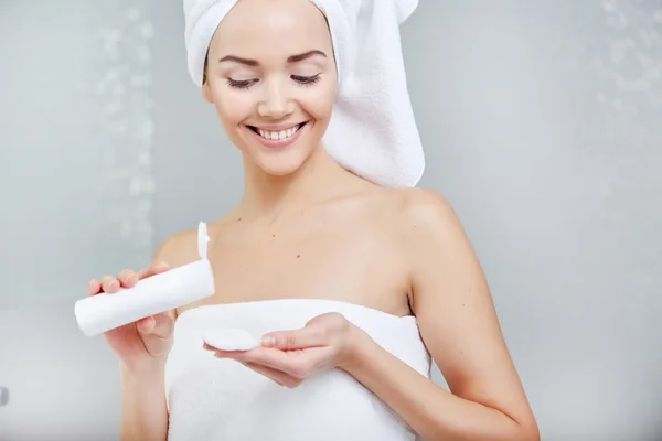 Mulher envolto com toalhas de banho, aplicando creme em seu rosto — Fotografia de Stock