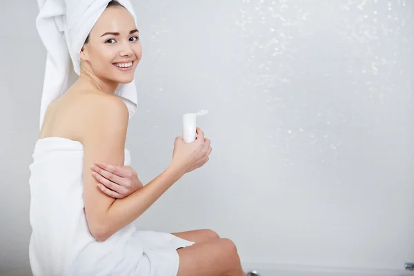 Mujer envuelta con toallas de baño, aplicación de crema en su cara — Foto de Stock