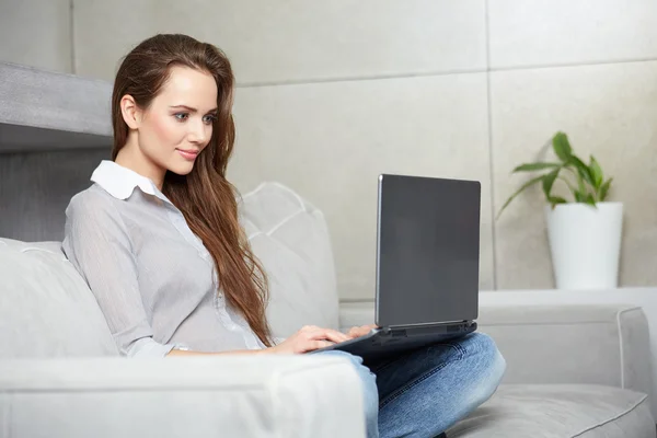 Egy nő laptopot használ, miközben a kanapén pihen. — Stock Fotó