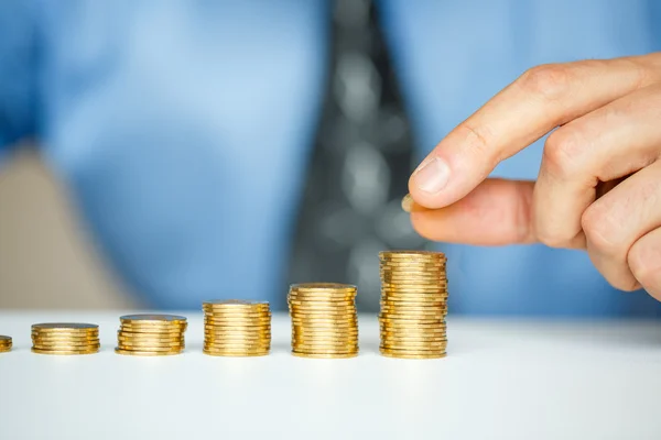 Mano masculina apilando monedas de oro en columnas crecientes — Foto de Stock