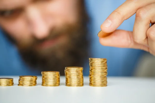 Bärtiger Mann stapelt Goldmünzen in zunehmenden Säulen — Stockfoto