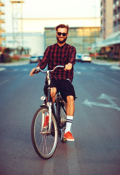 Stylish man in sunglasses riding a bike on city street — Stock Photo, Image