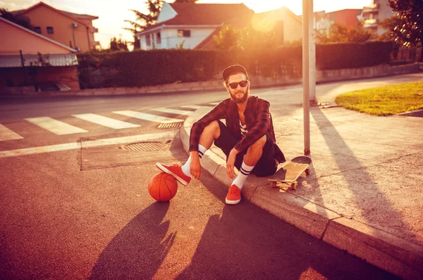 Stijlvolle man in zonnebril met een basketbal en skateboard — Stockfoto