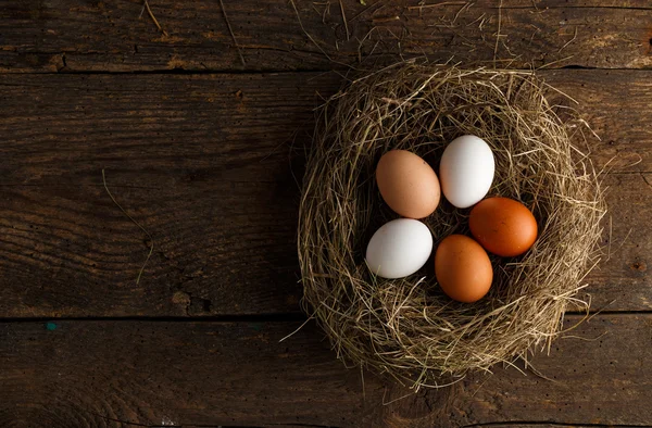 Fresh chicken eggs in a nest on a wooden background — Stock Photo, Image