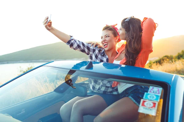 Duas meninas bonitas jovens estão fazendo selfie em um conversível — Fotografia de Stock