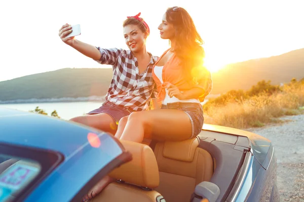 Two young beautiful girls are doing selfie in a convertible — Stock Photo, Image