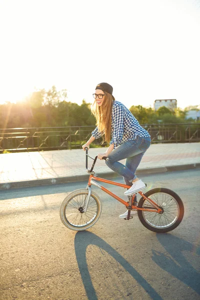 Härlig ung kvinna i en hatt cykla på staden bakgrund — Stockfoto
