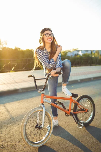 Adorável jovem mulher em um chapéu montando uma bicicleta no fundo da cidade — Fotografia de Stock