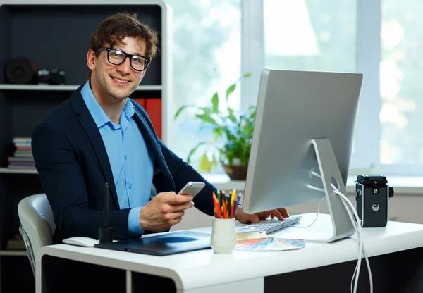 Joven guapo trabajando desde la oficina en casa y usando un teléfono inteligente —  Fotos de Stock