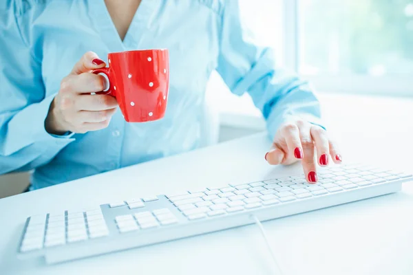 Trabajadora de oficina escribiendo en el teclado y tomando café — Foto de Stock