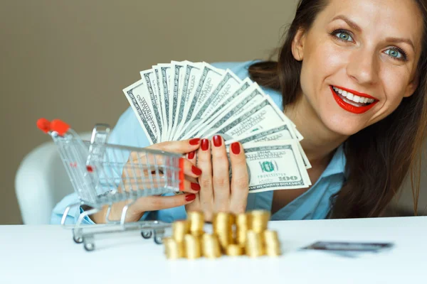 Joven mujer sonriente sosteniendo efectivo, y en la mesa hay monedas, cr —  Fotos de Stock