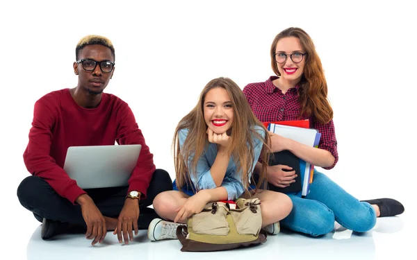 Three students sitting with books, laptop and bags isolated on w — Stock Photo, Image