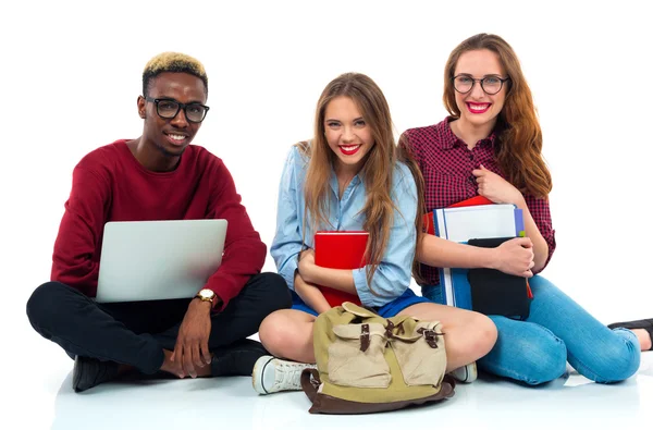 Tres estudiantes sentados con libros, portátil y bolsas aisladas en w — Foto de Stock