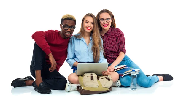 Tre studenti seduti con libri, laptop e borse isolate su w — Foto Stock