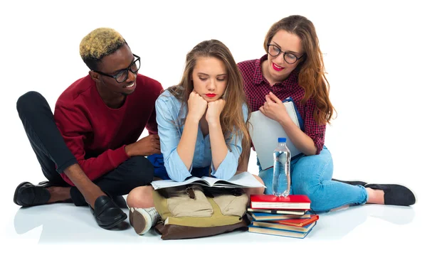 Three students sitting with books, laptop and bags isolated on w — Stock Photo, Image