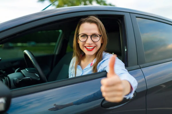 Joven mujer feliz sentada en un coche con las llaves en la mano y — Foto de Stock