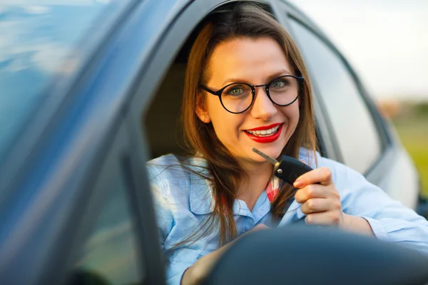 Jovem mulher bonita sentada em um carro com as chaves na mão — Fotografia de Stock