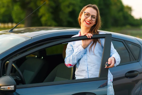 Mujer joven de pie cerca de un coche con llaves en la mano —  Fotos de Stock