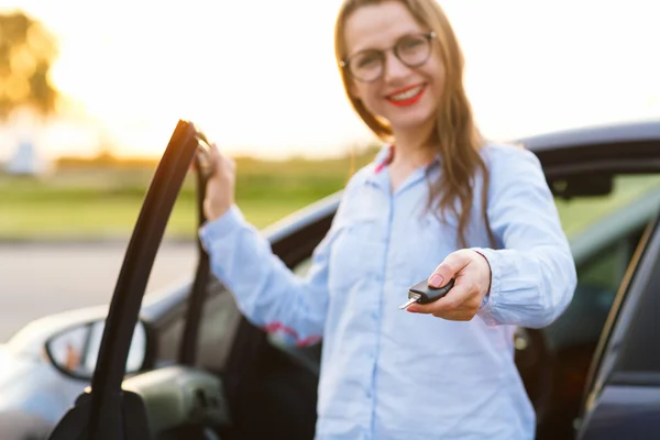 Mujer joven de pie cerca de un coche con llaves en la mano —  Fotos de Stock