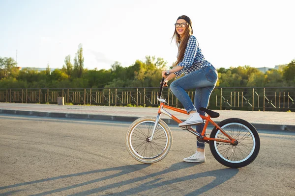 Härlig ung kvinna i en hatt cykla på staden bakgrund — Stockfoto