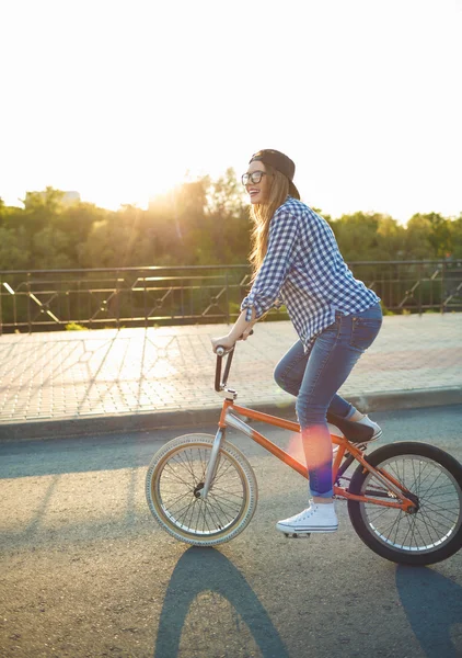 Mooie jonge vrouw in een hoed een fiets op de achtergrond van de stad — Stockfoto