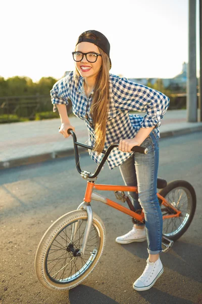 Härlig ung kvinna i en hatt cykla på staden bakgrund — Stockfoto