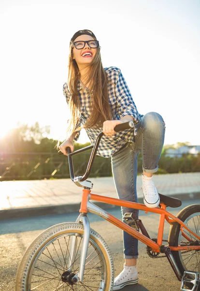 Preciosa mujer joven en un sombrero montando una bicicleta en el fondo de la ciudad — Foto de Stock