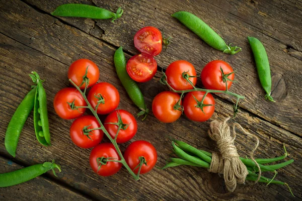 Frische Tomaten mit Spargel und grünen Erbsen auf einem hölzernen Backgro — Stockfoto